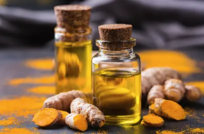 Fresh turmeric root beside small glass vials of golden curcumin extract