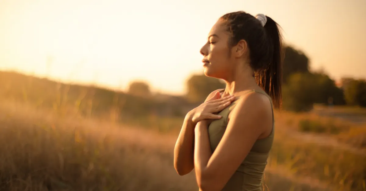 Woman breathing deeply outdoors at sunset with a hand on her chest